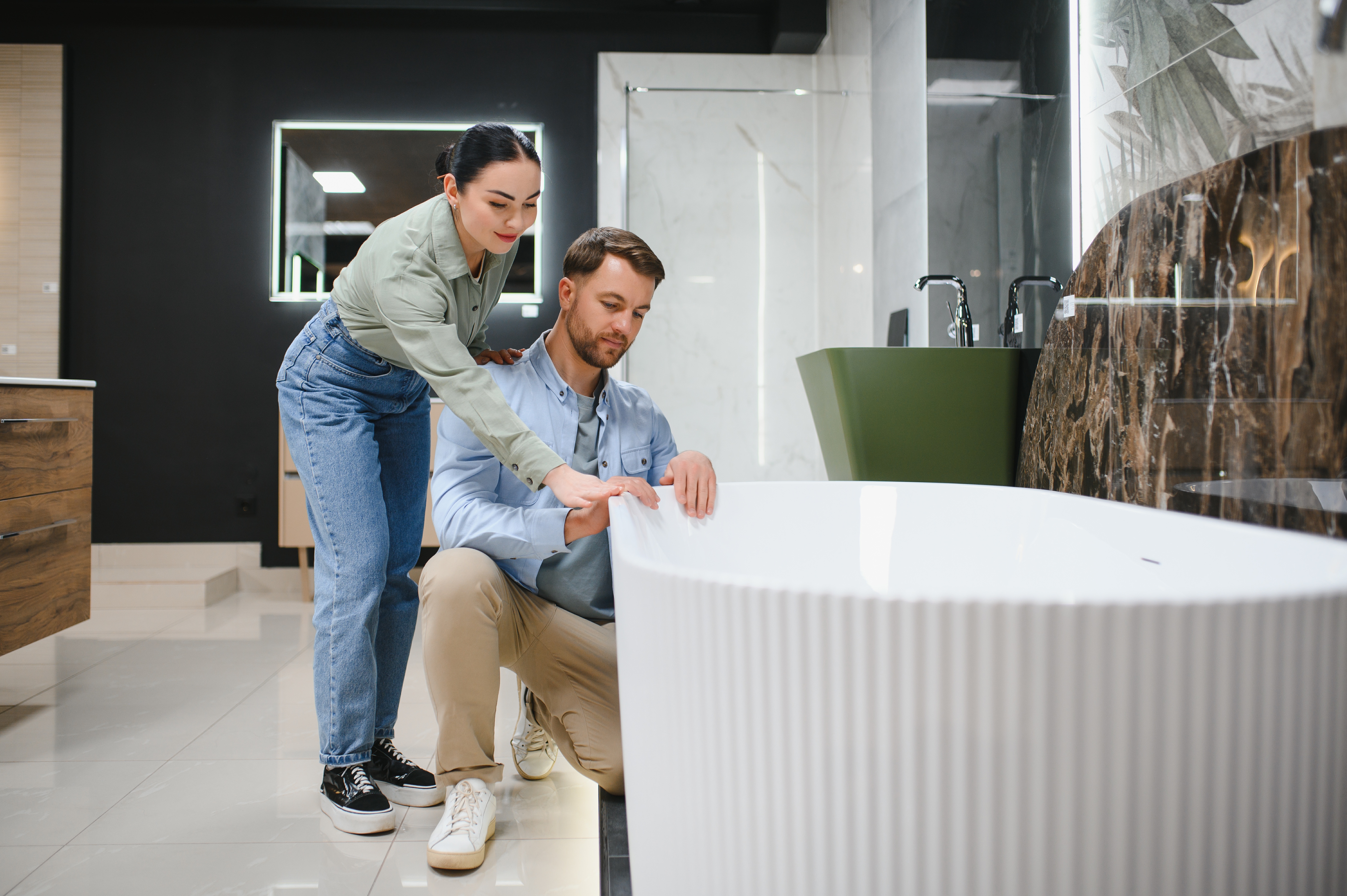 Casal em loja de produtos para banheiro, examinando de perto uma banheira branca moderna, com a mulher apontando para detalhes enquanto o homem observa.