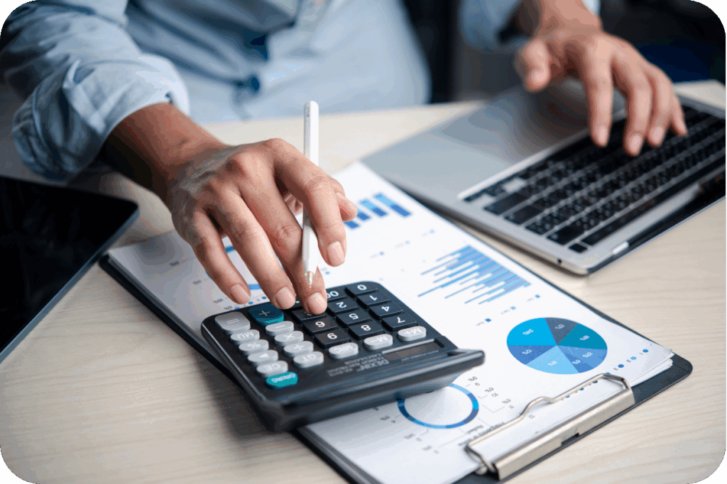 Mãos usando calculadora sobre relatórios e gráficos de previsão de custos de obra, simbolizando planejamento financeiro de projeto.